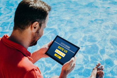 Yüzme havuzunda elektronik tabletle çevrimiçi bir hizmeti veya ürünü değerlendiren adam.