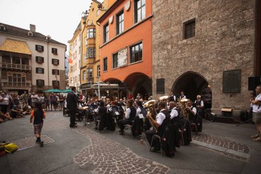 Innsbruck, Avusturya - 17 Ağustos 2022: Sokağın ortasında turistlerin dinlediği bir konser veren müzik orkestrası ve arka planda altın çatı binası