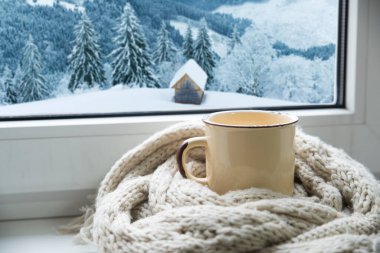 Sıcak kış durgun yaşamı: bir kupa sıcak çay ve dışarıdaki kar manzarasına karşı modern pencere pervazında sıcak ekose ile açılan kitap. Seçici odaklanma. Yüksek kalite fotoğraf