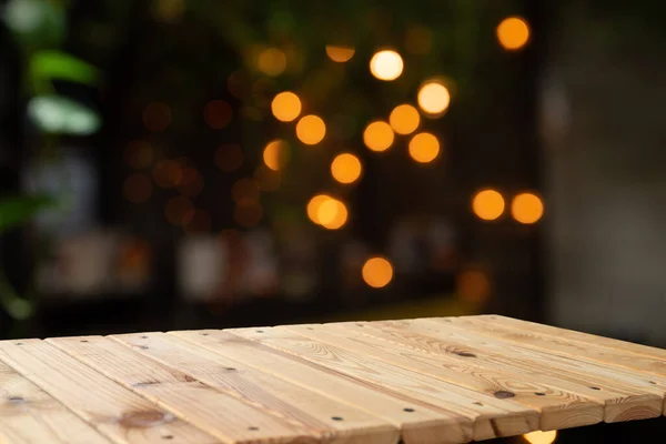Empty wooden table in front of blurred cafe bar or restaurant. Abstract lights bokeh background, front view, free space for your product. High quality photo