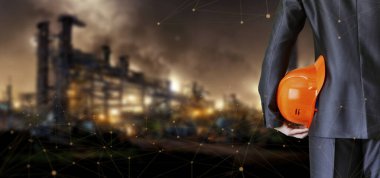 An engineer with a helmet in his hands stands in front of industrial production.