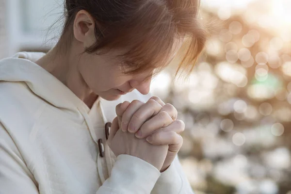 A woman prays with her head bowed against a blurred background.