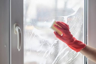 Temizlikçi kadın lastik eldivenli bir süngerle pencereyi yıkıyor..