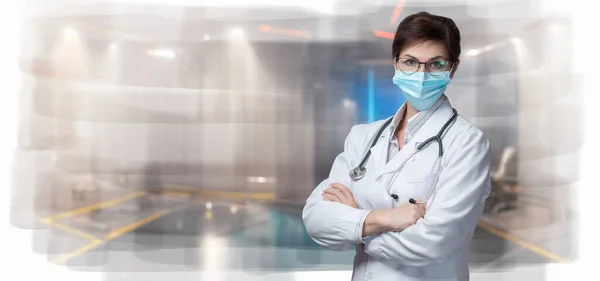 A doctor in a mask with his arms crossed on a blurred background.