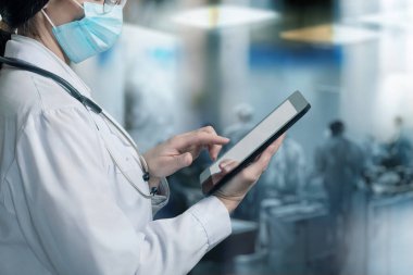 Doktor hastanenin arka planında bir tablet üzerinde çalışıyor..