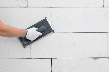 Bir işçi gaz bloğu duvarını bir aletle ovuyor. İnşaat işi kavramı.