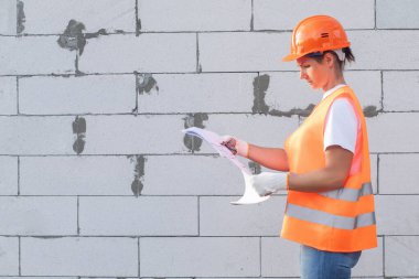 Projeyi gaz bloğunun arka planında inceleyen üniformalı bir inşaatçı.