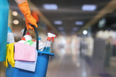 A cleaning lady with a bucket and cleaning products against the background of a blurred shopping center. clipart