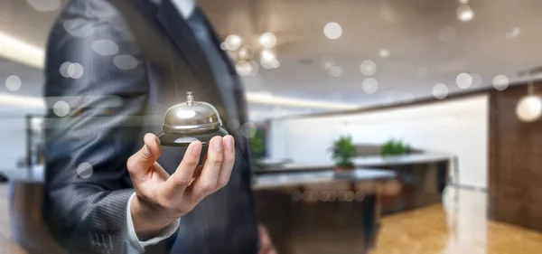 A hotel worker lies in his hands holding a bell against the background of a blurred reception.