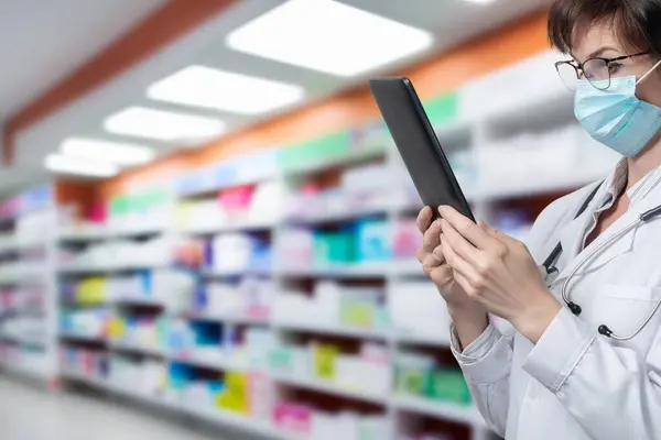 A pharmacist looks at a tablet computer against the background of a pharmacy.