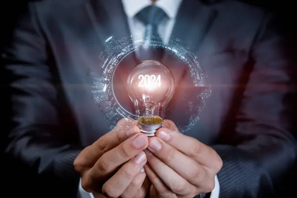 Concept of new ideas in the new year 2024. A man holds a light bulb with the glowing number 2024.
