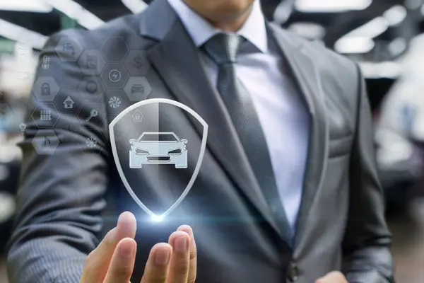 Auto insurance concept. A hand shows a shield with a car inside on a blurred background.