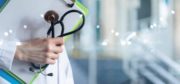 Doctor with stethoscope and folders of documents stands on a blurred background.