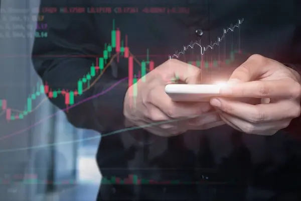 Trader performing analysis with a mobile device on a blurred background.