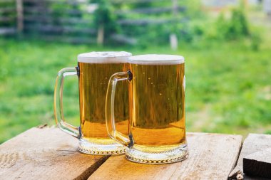 Ahşap bir masanın üzerinde bulanık bir arka planda iki bardak bira..