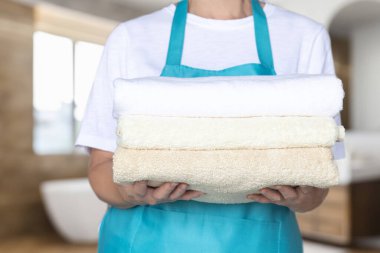 Önlüklü kadın temiz havluları banyoda tutuyor..