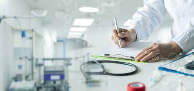 Modern bir klinikte masa başında oturan bir doktor not alır..