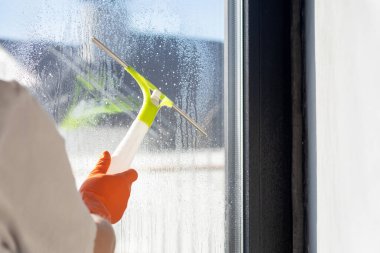 Temizlikçi kadın bir kazıyıcıyla pencereyi temizliyor. Pencereleri temizleme ve yıkama kavramı.