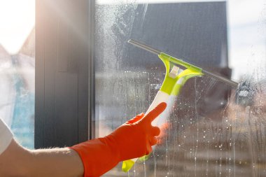 Temizlikçi kadın bir kazıyıcıyla pencereyi temizliyor. Cam temizleme ve yıkama konsepti.