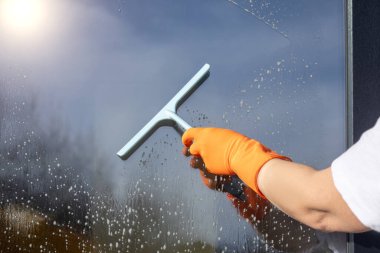 Temizlikçi kadın bir kazıyıcıyla pencereyi temizliyor. Cam yıkama konsepti.