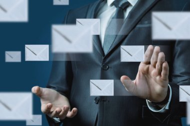 Resmi takım elbiseli bir işadamı şık bir ofis ortamında duruyor. Etrafında çeşitli e-posta zarfları uçuşurken dijital iletişim ve modern iş dinamikleri öneriyor..