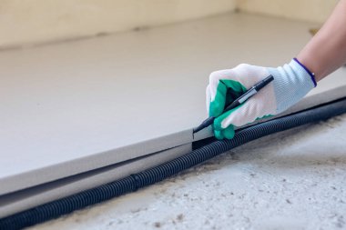 Bir işçi inşaat sahasında bir polistiren substratı dikkatlice işaretliyor ve zemin ısıtma sistemi kurulumuna hazırlanıyor. Bu süreç uygun yalıtım ve ısıtma verimliliği sağlar.