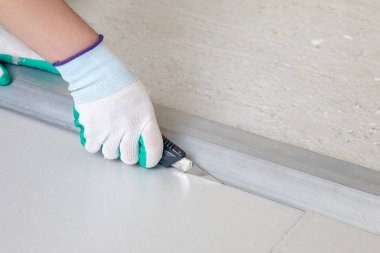 Bir işçi zemin yüzeyindeki yalıtım malzemelerini kesmek için bıçak kullanıyor, düzgün yerleştirme ve inşaat sürecine uyması için hassas ölçümler yapıyor..