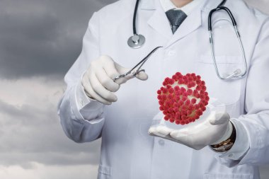 Beyaz önlüklü bir tıp uzmanı laboratuvarda kırmızı virüs modelini incelemek için forseps kullanır. Arka plan, sağlık araştırmalarında aciliyeti simgeleyen dramatik bir gökyüzünü gösteriyor..