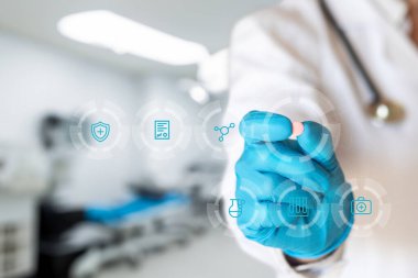 Eldivenli bir sağlık uzmanı tıbbi simgelerle dolu sanal bir ekranla etkileşime girerken bir tablet gösterir. Bu, tıbbi teknoloji ve hasta bakımında yenilikler sergiliyor..