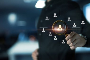 Bir kişi, modern ofis ortamındaki adayları temsil eden dijital simgelerin üzerinde bir büyüteç tutuyor. Eylem, askere alma faaliyetlerine odaklanılmasını öneriyor.