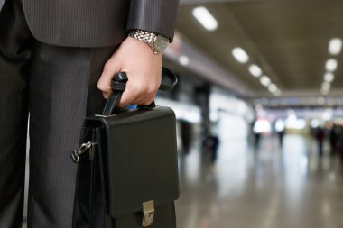 İş gezgini havaalanında bir uçuş için hazırlanıyor. Profesyonel bir adam elinde çantayla havaalanında duruyor ve ilerideki yolculuğuna odaklanıyor..