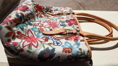 Çiçek desenli ve kahverengi elli el çantalı kadın aksesuarı. Beyaz el çantasına çok renkli çiçek tasarımları