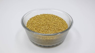 Beyaz zemin üzerinde şeffaf kâse içinde sarı hardal tohumları.