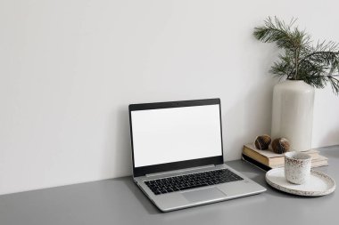 Noel ofisi hala hayattadır. Laptop, bilgisayar modeli. Boş ekran. Bir fincan kahve, vazoda çam ağacı dalları, gri masada Noel süsleri, İskandinav şenlikli kış evi dekorasyonu..