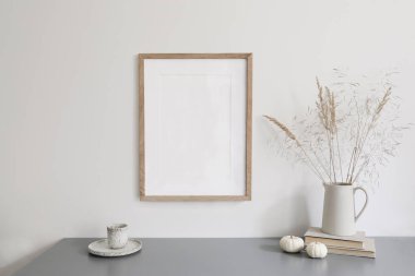 Sonbahar kahvaltısı hala hayat sahnesi. Kuru otlu seramik sürahi, bir fincan kahve. Beyaz küçük balkabakları, gri masa. Boş ahşap çerçeve modeli, İskandinav iç mimarisi, boho evi. Şükran Günü Dekorasyonu