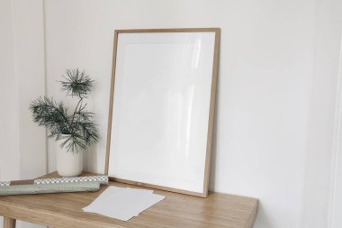 Noel 'in içinde hayat var. Boş tahta çerçeve, ahşap masa, masa. Vazoda çam ağacı dalları. Boş kağıt çarşaflar, masanın üstünde hediye paketi, beyaz duvar arkaplanı..