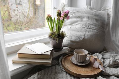 Cozy Easter, spring still life scene. Cup of coffee, books and blank greeting card on windowsill. Vintage feminine styled photo. Moody floral composition. Potted pink hyacinth flowers, linen plaid.