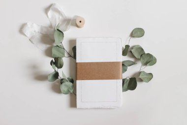 Blank notepad mockup. Cotton paper diary with rough edges, craft belly band, tape isolated on white table background. Dry eucalyptus leaves, branch, wedding composition, office supply. Flatlay, top.
