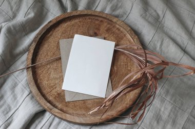 Boho düğün davetiyesi. Tahta tepside boş bir tebrik kartı modeli. Kuru palmiye yaprağı. Bej rengi pamuklu kumaş, battaniye. Tropik yaz kırtasiyesi şablonu, tasarım, düz döşeme, üst görünüm, insan yok.