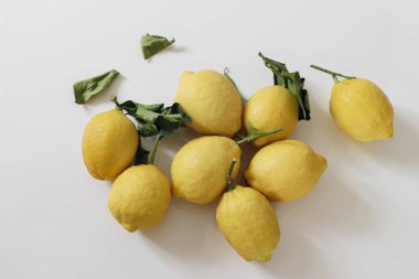 Fresh yellow lemons, dry green leaves isolated on white background. Mediterranean juicy fruit on table. Healthy eating concept. Summer natural food still life. Flat lay, top view, no people.