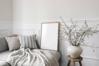 Modern bahar İskandinav oturma odasının iç kısmı. Ahşap çerçeve, poster modeli. Keten, mavi çizgili yastıklı kanepe. Vazoda kiraz çiçekleri, zarif stil ev dekorasyonu..