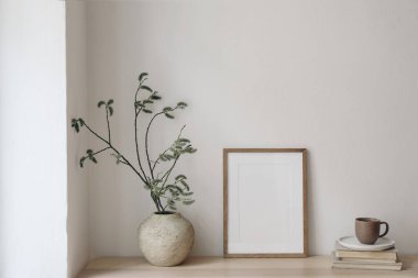 Kahvaltı hala hayattadır. Modern oturma odası. Bir fincan kahve, kitaplar. Boş ahşap çerçeve masanda, masada. Yeşil söğüt ağacı dallı vazo, zarif Scandi çalışma alanı, ev ofisi..
