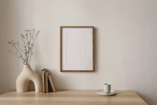 stock image Empty wooden picture frame mockup hanging on beige wall background. Boho shaped vase, dry flowers on table. Cup of coffee, old books. Working space, home office. Art, poster display, modern interior.