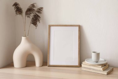 Boş tahta, dikey çerçeve modeli. Kuru kamışlı vazo, masada çimen, masa. Bir fincan kahve, kitaplar. Zarif bir iç mekan, ev ofisi. Dekoratif boho natürmort fotoğraf, sanatsal poster görüntüsü.