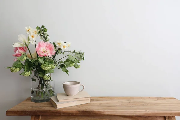 ムーディ スプリングはまだ生きてる 木製のベンチ コーヒー 古い本のカップとテーブルの組成 ピンクのチューリップ 水仙と美しい花の花束 ホーソン 緑のゲラーバラの花 — ストック写真