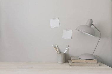 Lamba, kitap ve kalem tutacağı olan ahşap masa. Duvara yapıştırılmış not defterleri. Tarafsız stil minimum çalışma alanı. Bej arkaplan, boş kopya alanı. Merkez ofis konsepti. Yaşam tarzı pankartı.