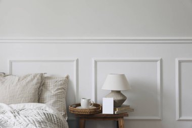 Klasik klasik yatak odası iç mimarisi. Hasır tepside kahve, ahşap bankta masa lambası. Boş tebrik kartı, davetiye maketi, beyaz duvar arka planı. Yatak takımı, yastıklar..