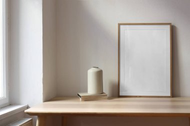 Modaya uygun bir iç mekan. Oturma odasında seramik vazo, pencerenin yanındaki ahşap masada eski kitaplar. - Evet. Boş ahşap çerçeve, poster modeli. Ev dekorunun minimalist konsepti, İskandinav tasarımı.