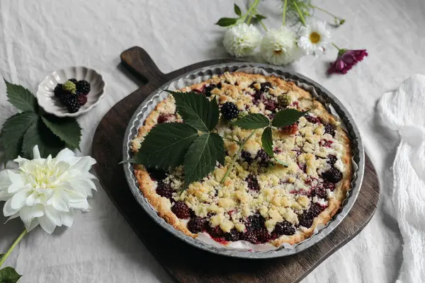 Food, kitchen still life. Homemade sweet blackberry pie, tart. Old wooden chopping board. Bowl with berries on table. Grey linen table cloth. Breakfast, baking concept. Dahlia flowers, flat lay, top