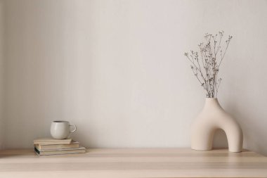 Bir fincan çay, eski kitaplarda kahve. Kuru çiçekli, otlu modern organik vazo. Evdeki tahta masa. Minimal Scandi boho iç mekanı. Bej duvar arka planı. Boş kopyalama alanı. Oturma odası modeli.